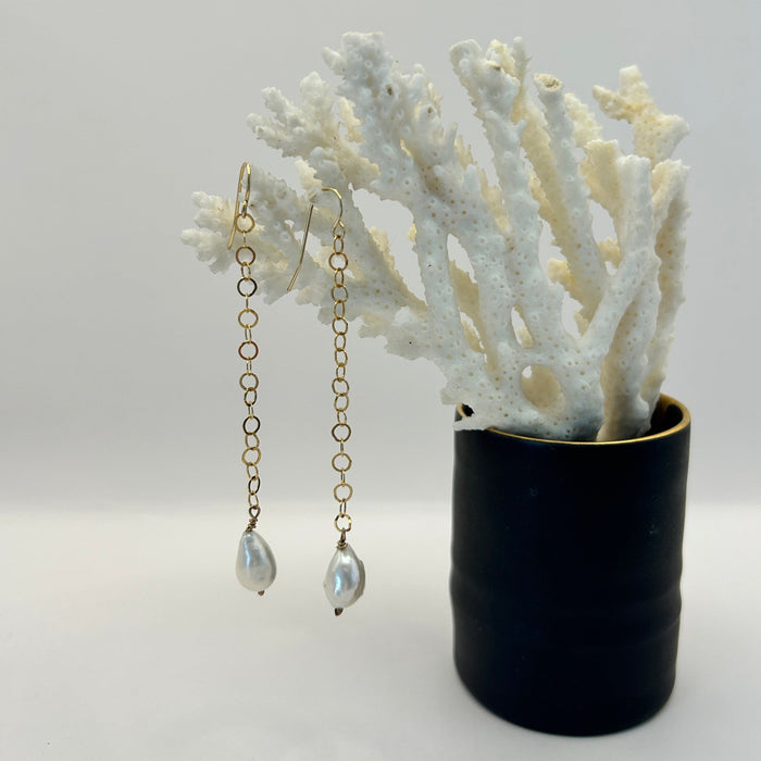 Gold earrings with pearl drops by Badgers Velvet displayed on a white coral branch against a light background.