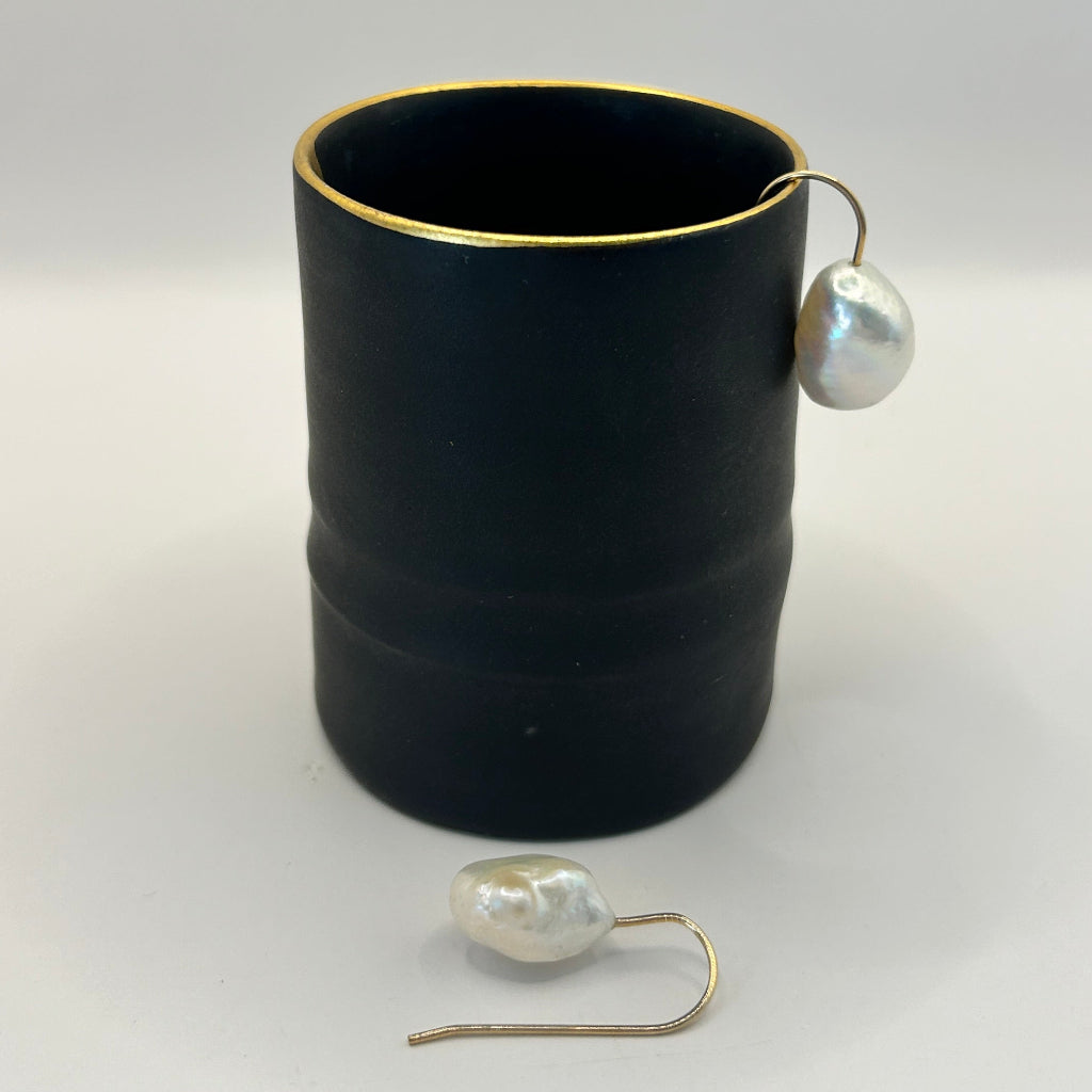 Baroque pearl hook earrings against a pot by ceramicist Fliff Carr