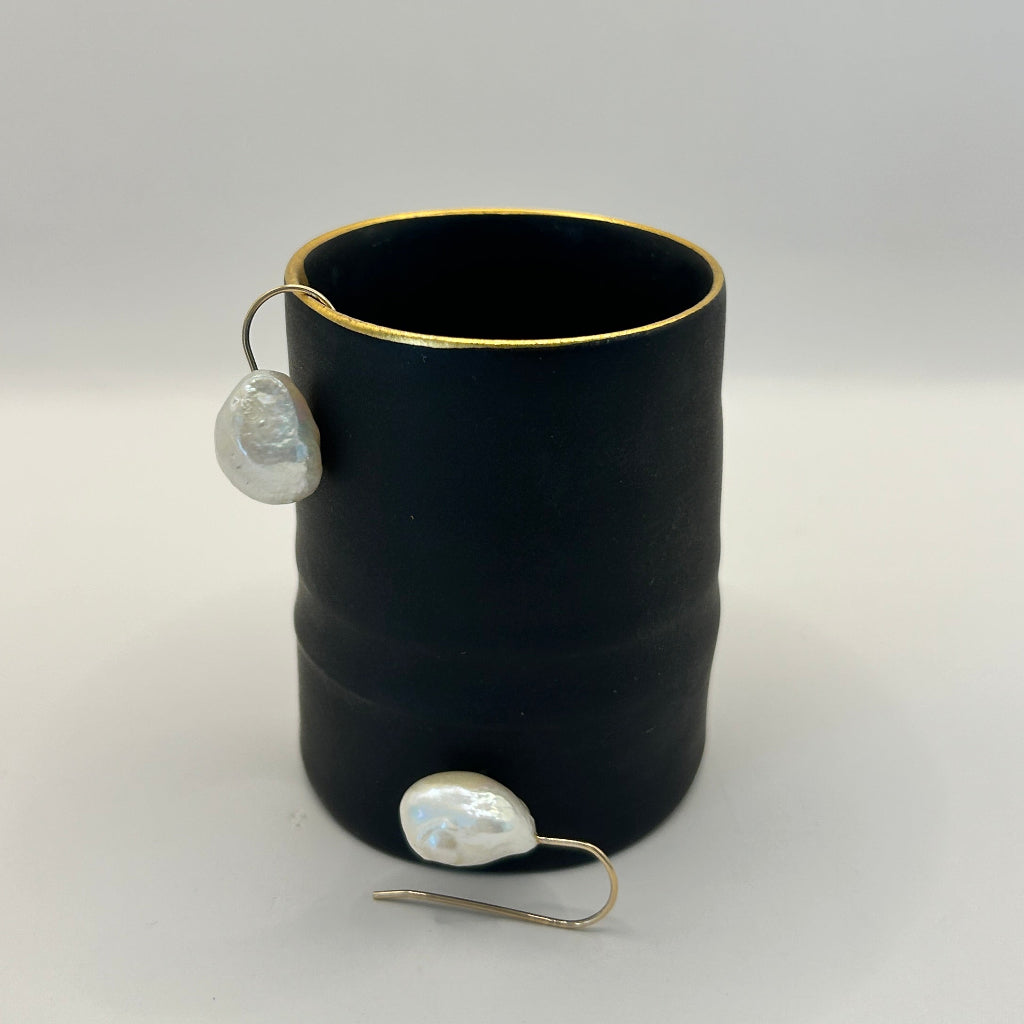 A pair of Baroque pearl hook earrings against a pot by ceramicist Fliff Carr